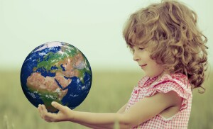 Child holding Earth in hands against green spring background. Elements of this image furnished by NASA